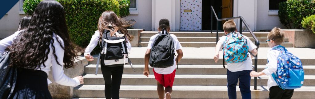 Un gruppo di bambini, con lo zaino in spalla, corre verso l'ingresso della scuola